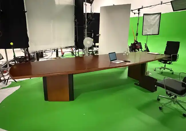 Used 14-foot mahogany-colour boat-shaped boardroom table on a film production set with green screen backdrop.